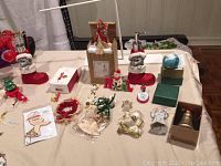 Photo showing assortment of Christmas ornaments including red Santa boots, small figurines, wreath, angel ornaments, a ceramic globe ornament, and boxed items on table.