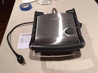 Closed view of the Breville panini grill showing the stainless steel top, power cord, and temperature dial.