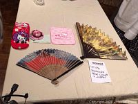 Full lot on table including two fans, Hello Kitty socks, cleaning towels, sponge, and mini hat keychain