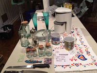 Wide view of all kitchen items arranged on a table, showing glass containers, ceramic mugs, knives, pepper mill, and magnets.