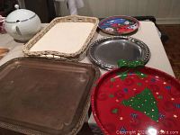 Multiple serving trays and glass cutting board displayed on table, shows condition and wear especially on the large metal tray and festive tray.