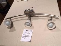 Full view of the curved chrome kitchen light fixture with three glass-shaded lamps on a table.