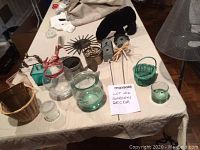 Assorted garden decor items displayed on table including glass jars, wicker baskets, decorative birdhouses on sticks, and metal decor pieces.