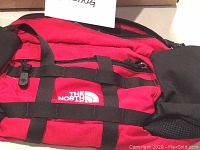 Front view showing The North Face logo, red fabric with black straps and side drink holders.
