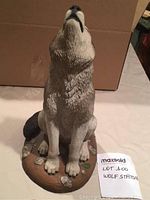 Front view of the grey and black wolf statue sitting on an oval base, showing the wolf's head raised upward.