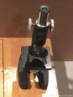 Front angled view of black antique children's microscope showing eyepiece and fine/coarse focus knobs