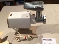 Oster electric meat grinder showing white plastic body, beige base, metal grinding tray and front grinding plate.