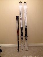 Full view of Atomic skis with mounted bindings alongside Grable poles leaning against wall