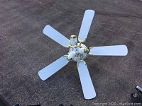 Top-down view of the white ceiling fan with five blades and five light fixtures on ground surface.