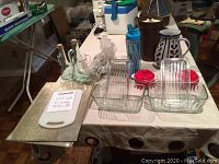 Wide shot displaying all kitchen items on table including glass meatloaf molds with lids, red small molds, oil and vinegar bottles, plastic pitcher, water bottles, mini cutting board, and ceramic pitcher.