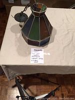 Overall view of the small antique Tiffany style pendant lamp showing stained glass panels and metal hanging chain.