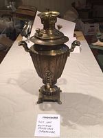 Full view of antique Russian charcoal samovar on a table showing entire item with handles, spigot and base.
