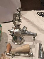 Manual metal fruit presser with clamp and wooden handle on white cloth, alongside a pestle.