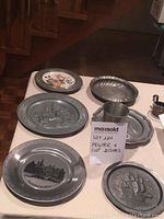 Full set of four pewter dishes, pewter cup, and two marble candle holders arranged on table showing designs and stamped marking