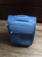 Blue carry-on suitcase viewed from top down showing front pocket and zipper.