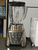 Full view of Oster blender with glass pitcher and black lid on stainless steel base with control panel buttons visible