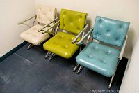 Photo showing three vintage armchairs arranged side by side against a wall, highlighting padded vinyl upholstery and chrome frames.