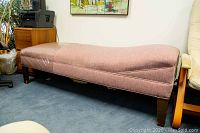 Side view of the dusty rose upholstered chaise lounge showing the length, shape and wooden legs.