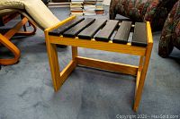 Side angle view of wooden side table showing light-colored frame and black slatted top, placed on carpet with chairs nearby
