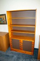 Teak bookcase with four shelves and two panel doors with circular cutout handles at the bottom, shown from front angle.