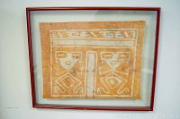 Front view showing the framed cloth with detailed geometric and animal motifs in orange and white, inside a dark wooden frame and under double glass.