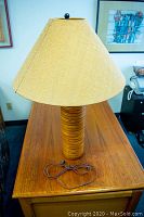 Full view of lamp on wooden table showing layered wood base, tan fabric shade and cord.