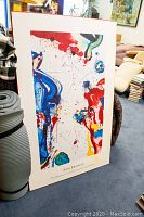Full view of Sam Francis abstract poster with characteristic splashes of color and backing board, placed upright in a room.