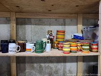 Shelf with various mugs, including brown, black, white with colored stripes, and stacked multi-coloured striped mugs