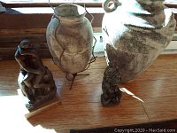 Photo showing two pottery jugs and two sculptures together on wooden floor with lighting from window.