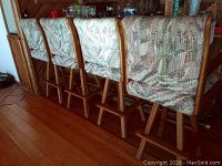 Side and back view of four upholstered bar stools lined up together showing patterned fabric upholstery and wooden legs with footrests.