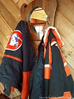Mirrored wall hanger with three Denver Broncos winter jackets hanging on hooks showing their logos and tag attached