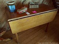 Handcrafted wooden drop leaf table with items on top including a planter pot and cloth pouch