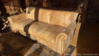 Front three-quarter view of tan distressed leather sofa with rolled arms and brass nailhead trim.