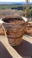 Single large round concrete planter with weathered surface and pine needles inside, shown on outdoor patio with natural background