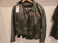 Black leather jacket with fringe and red floral embroidery hanging on hanger