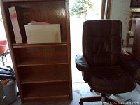 Oak wood bookcase with shelving and box on middle shelf, also showing black office chair positioned beside it.