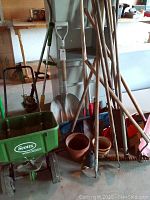 Wide view showing assorted garden tools including Scott's fertilizer spreader, rakes, shovels, pots, and a cordless weed whacker.