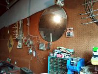 Photo showing pegboard with hanging hand tools, small hardware packages, green and blue plastic hardware organizer drawers, and a round framed wall mirror.