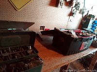 Three toolboxes on a workbench including a green metal toolbox filled with bolts, screws, and hand tools along with a black toolbox and other tools.