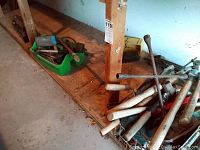 Three crates on lower wooden shelf containing various hand tools like hammers and some hardware in green container and wire basket