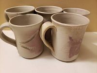 Five handcrafted pottery mugs grouped with focus on design and handles to show uniqueness and craftsmanship.