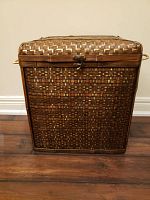 Front view of the closed woven hamper basket showing textured pattern, metal clasp, and side handles.