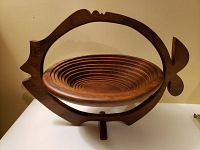 Wooden expanding bowl resting on a fish-shaped wooden frame with tripod stand, shown from front angle.