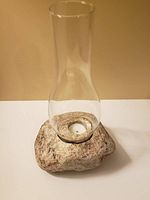 View of the entire candle holder showing natural rock base and clear glass chimney with a tea light candle inside.