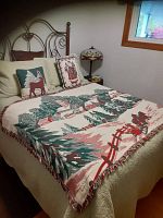 Bed with Christmas-themed living room showcasing two woven throw blankets in green-cream and red-cream colors, plus two matching decorative pillows with reindeer and Santa Claus.
