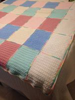 Full view of the crocheted afghan blanket laid out, showing patchwork of pastel color squares in pink, cream, blue, and green.