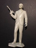 Full view of white plastic figurine of Illya Kuryakin holding scoped rifle, standing upright with base.