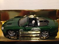 Side view of green diecast Jaguar convertible with black interior and villain Zao figure seated inside, mounted on gold packaging base.