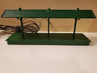 Side view of green Lionel model train station platform with roof and attached wires.