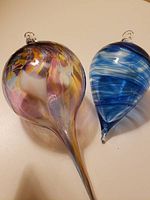 Two handblown glass ornaments on a flat surface, showing their colors and shapes.